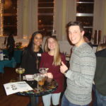 Image of two women and one guy standing at a table with drinks