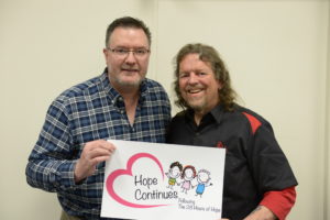 Image of Brian and Todd holding sign saying hope continues